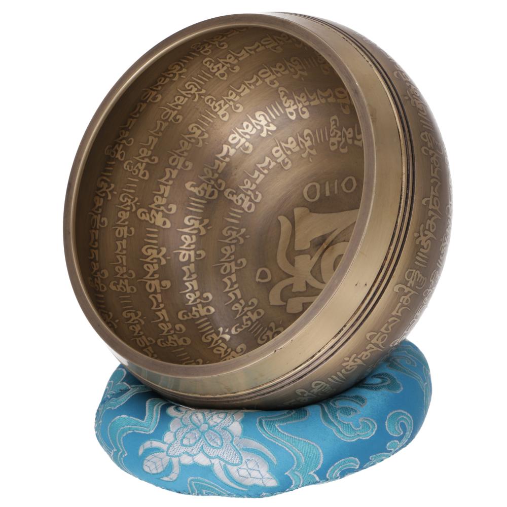 Tibetische Klangschale aus Bronze mit Om-Symbol und Mantra-Gravuren, auf einem blauen Klangschalenkissen mit Blumenmuster.
