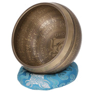 Tibetische Klangschale aus Bronze mit Om-Symbol und Mantra-Gravuren, auf einem blauen Klangschalenkissen mit Blumenmuster.
