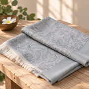 Wollschal Amritsari Water-Grey aus 100 % Wolle, fein gefaltet mit dezentem Paisleymuster und kurzen Fransen in elegantem Blau-Grau.