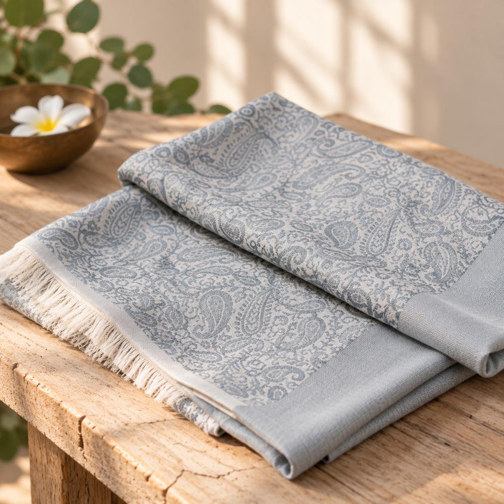 Wollschal Amritsari Water-Grey aus 100 % Wolle, fein gefaltet mit dezentem Paisleymuster und kurzen Fransen in elegantem Blau-Grau.