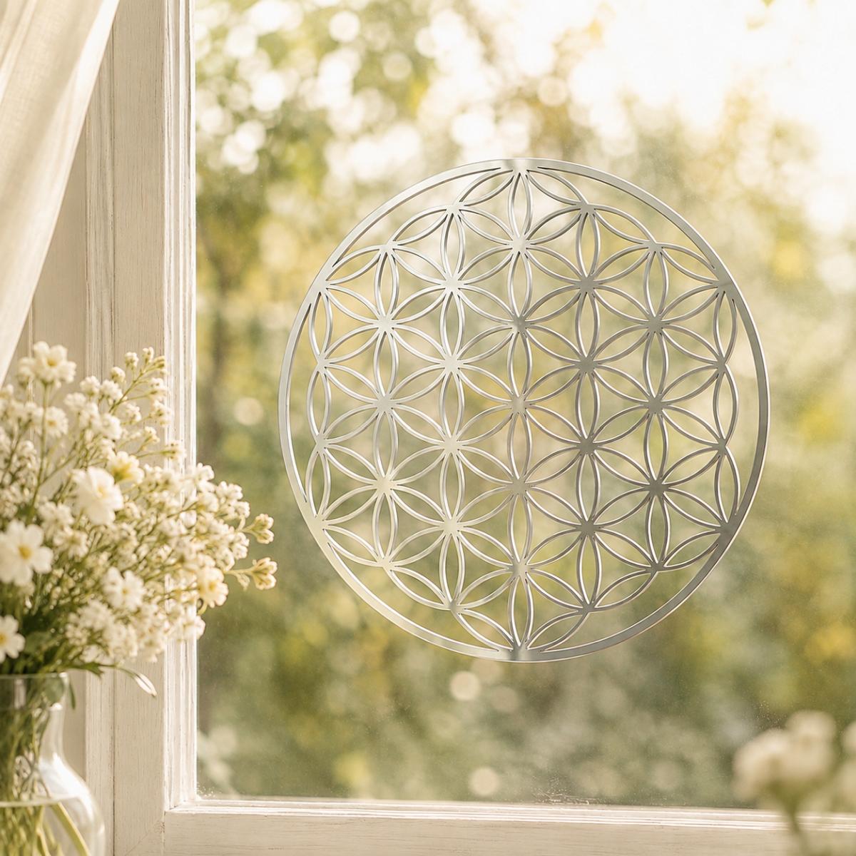 Silberfarbene Blume des Lebens aus glänzendem Edelstahl mit 18 cm Durchmesser als Fensterbild neben frischen weißen Blumen.