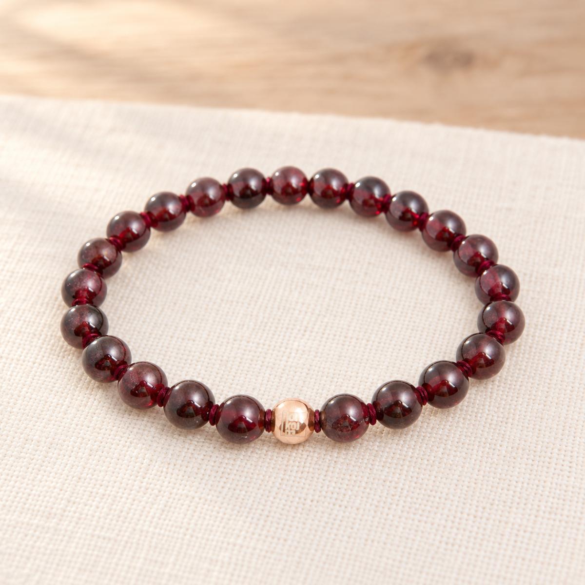 Granat Armband mit geknoteten Heilsteinperlen und roségoldfarbener Markenperle auf hellem Naturleinen